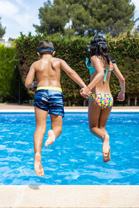 Two funny kid jumping into a swimming pool. back view.