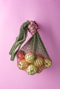 Close-up of hand holding apples in netting while coming out from torn paper 