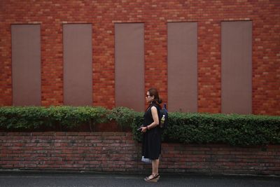 Full length of woman standing against brick wall