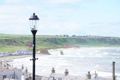 Street light by sea against sky in city