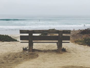 Empty bench on beach by sea against sky