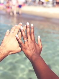 Cropped hands of couple wearing rings over sea