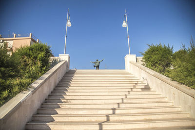 Low angle view of steps amidst buildings against clear blue sky