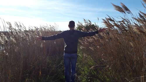 Rear view of man with arms outstretched standing on field against sky