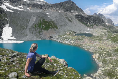 Rear view of woman sitting on rock by lake