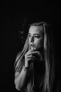 Thoughtful young woman smoking cigarette against black background