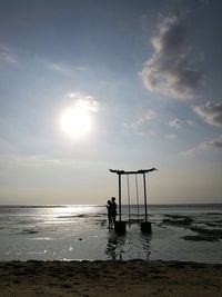 Man sitting on beach against sky during sunset