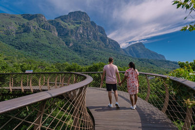 Rear view of couple walking on footbridge