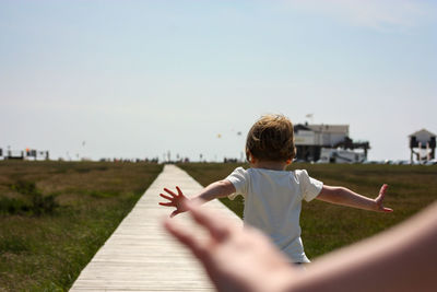 Rear view of boy running on footpath against sky