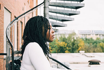 Side view of young woman standing against built structure