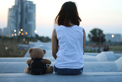 Rear view of woman with teddy bear sitting in city