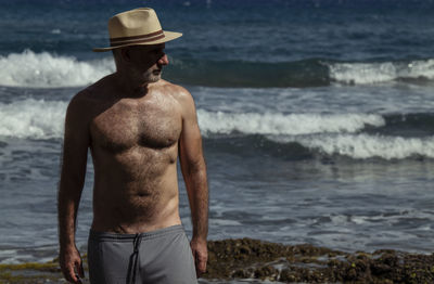 Portrait of shirtless man in hat against sea