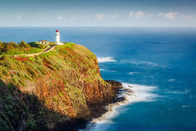 Lighthouse on cliff by sea against sky
