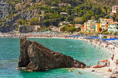 Imposing rock at the edge of the beach in the town of monterosso. many people swimming in the sea