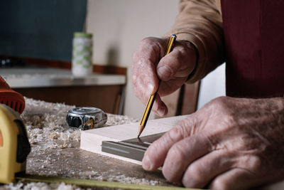 Cropped hands of carpenter measuring wooden plank in workshop