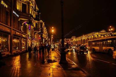 Vehicles on road amidst illuminated buildings against sky at night