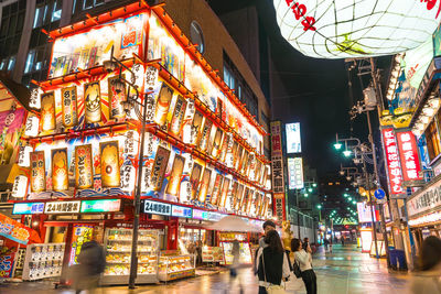 People walking on illuminated street amidst buildings in city at night