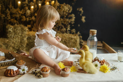 A little girl is sitting on the easter table and playing with cute fluffy ducklings.  happy easter.