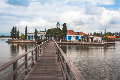 Pier over lake by buildings against sky