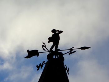 Low angle view of weather vane against cloudy sky