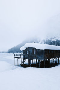 Cold winter landscape with lonely stilt house located near frozen river in snowy mountain valley in dense snowstorm