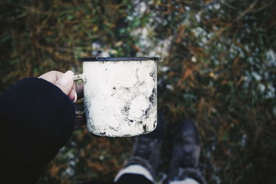 Close-up of woman hand holding dirty mug on field