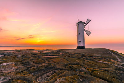 Lighthouse by sea against sky during sunset