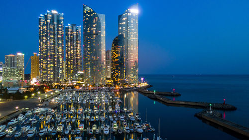 Illuminated modern buildings by sea against sky at night