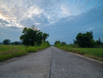 Empty road amidst field against sky