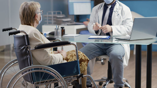 Disabled senior woman sitting on wheelchair discussing with doctor in clinic