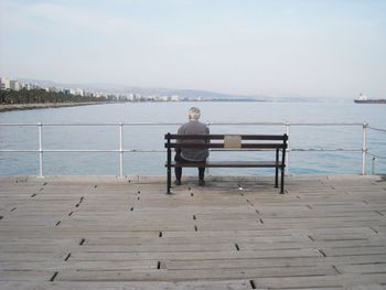 Rear view of senior man sitting on bench against sky