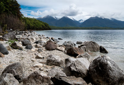 Rocky shore of lake with mountains in backdrop. lake manapouri, fiordland national park, new zealand