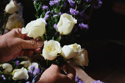 Close-up of woman hand holding white rose by purple flower in shop