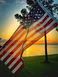 American flag by sea against orange sky