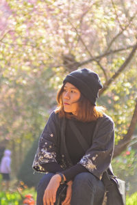 Young woman looking away while sitting on tree