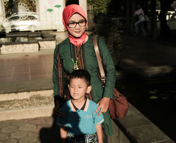 Woman with son standing against building on sunny day