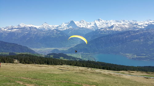 Person paragliding against mountains against clear sky