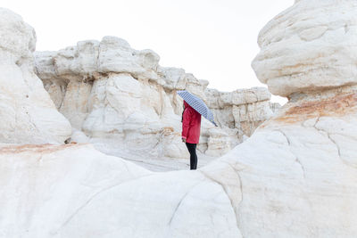 Woman in a red jacket standing in between rock formations holding an umbrella