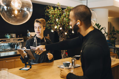 Male customer doing contactless payment through smart phone at coffee shop