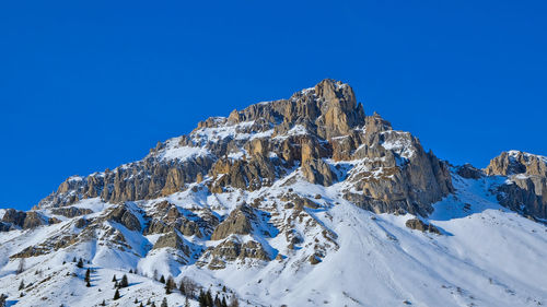 Low angle view of snowcapped mountains against clear blue sky