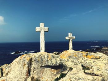 Cross on rock by sea against blue sky