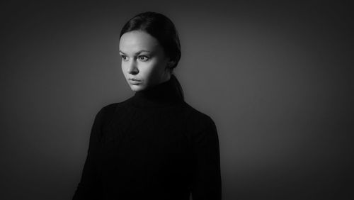 Young woman looking away while standing against gray background