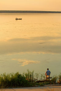 Rear view of man fishing at lake during sunset