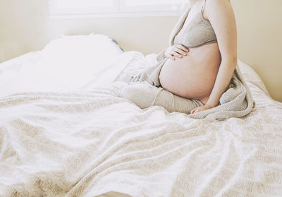 Midsection of pregnant woman sitting on bed at home