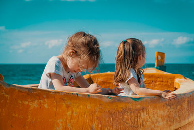 Siblings on boat in sea against sky