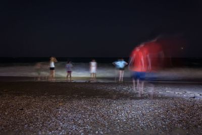 Blurred motion of people at beach against sky at night