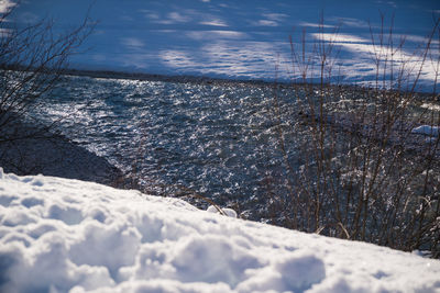 Snow covered land by sea against sky