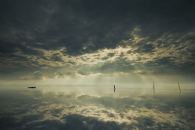 Silhouette man walking at beach against cloudy sky
