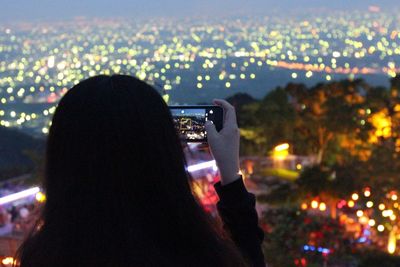 Rear view of woman photographing illuminated city at night