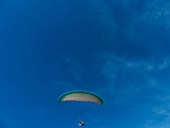 Low angle view of person paragliding against blue sky